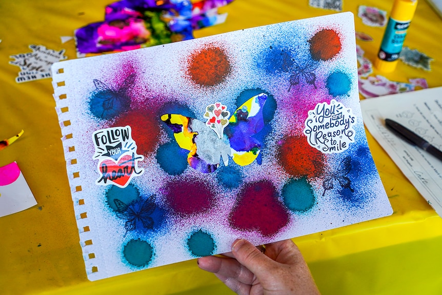 A hand holds up a colourful piece of paper with a butterfly motif and tie dye