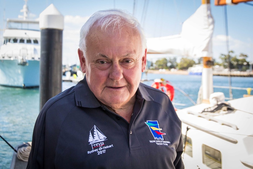 Dick Lees stands on a wharf in front of a yacht.