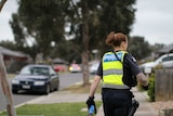 A female police officer is shown from behind walking down a suburban street, carrying pepper spray.