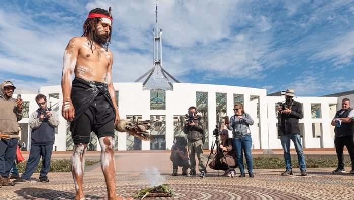 An aboriginal man stands before a fire at Parliament House in Canberra