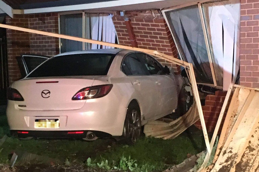 A white car crashed into a red brick house, badly damaging it.