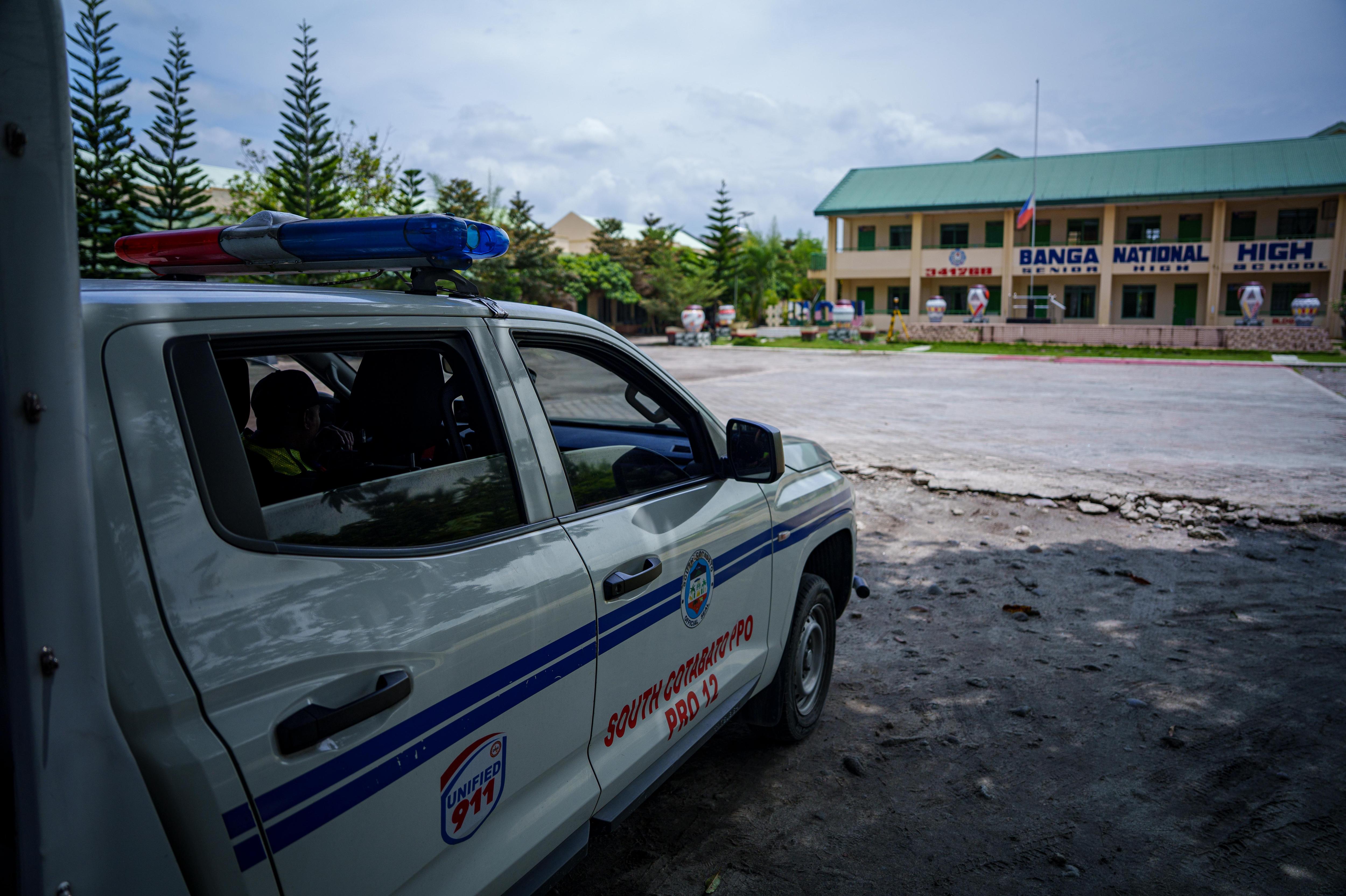 A Philippines police car is parked opposite the Banga National High School building on a sunny day.