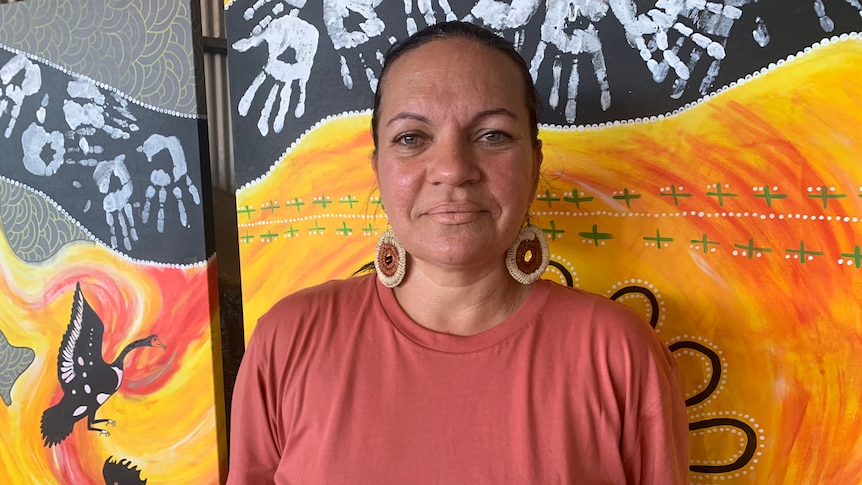 A woman stands in front of a wall with a mural on it