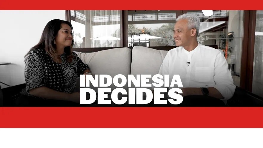 A woman interviews a man wearing white and sitting on a couch.