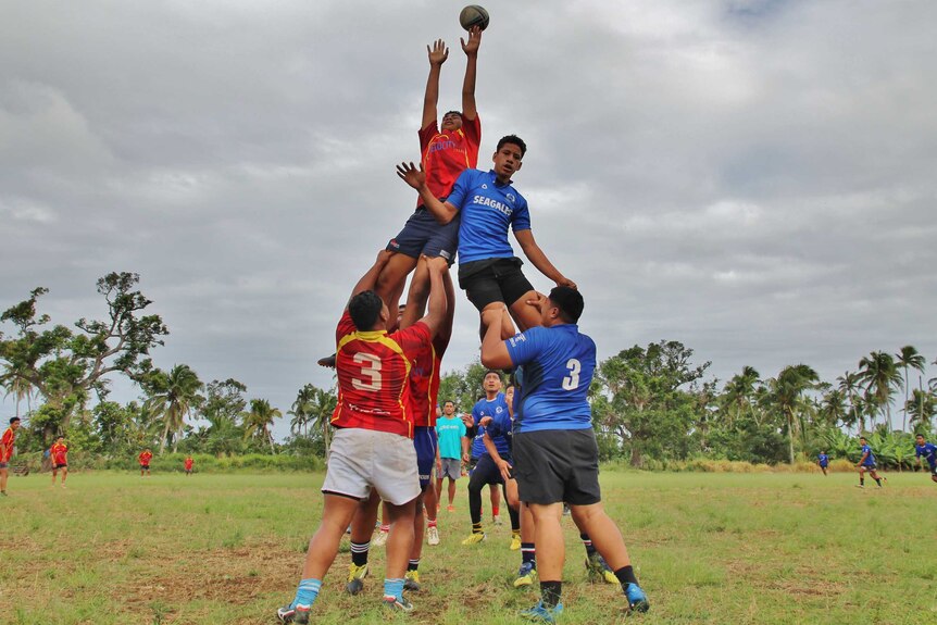 Two teenage rugby players are lifted high in a lineout but the ball is just beyond their reach.