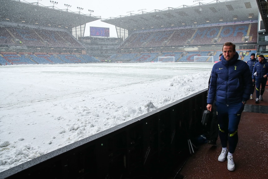 A Premier League star is bundled up in a parka as he walks alongside a snow-covered pitch