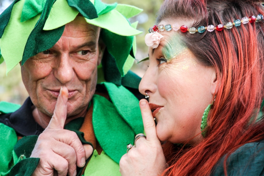 Two adults dressed as tree fairies make the "shoosh" gesture.