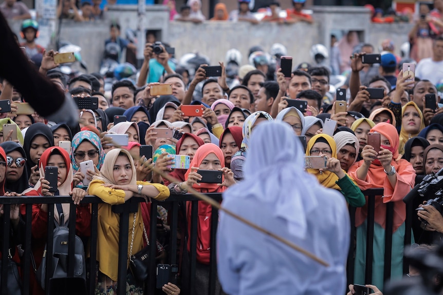 A person in white can be seen knelling as crowds of people hold up their phones.