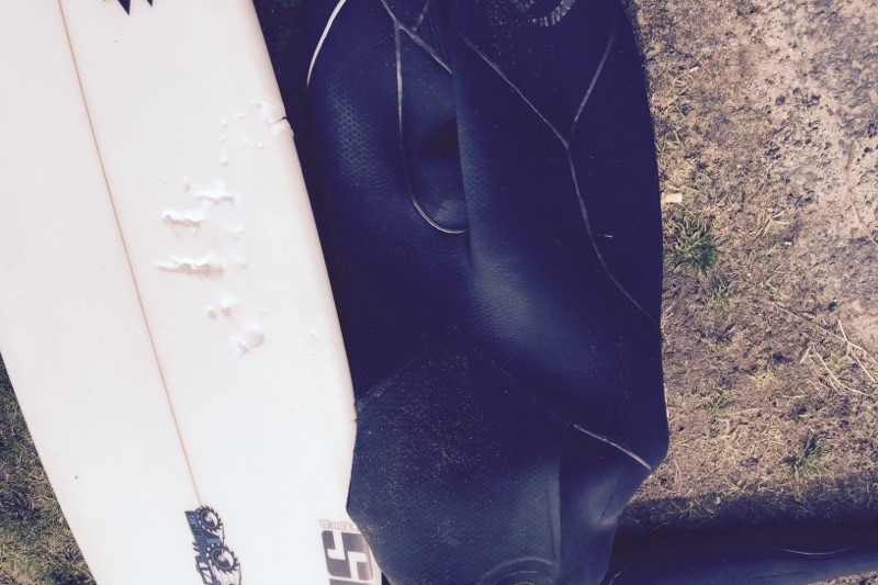 A surfboard with shark bite marks in it, next to a winter wetsuit.
