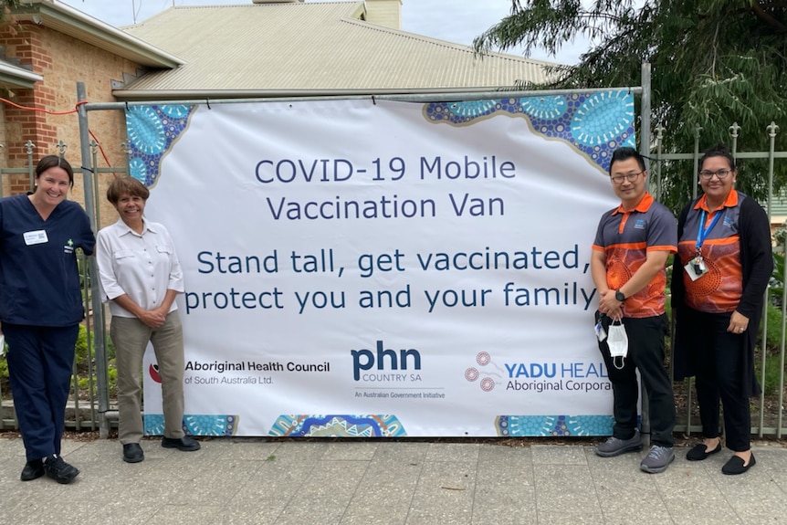 Two people stand on either side of a white banner promoting their covid-19 vaccination van