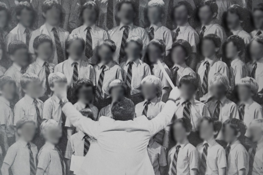 A group of young choir boys standing in rows directed by a conductor, in black and white.