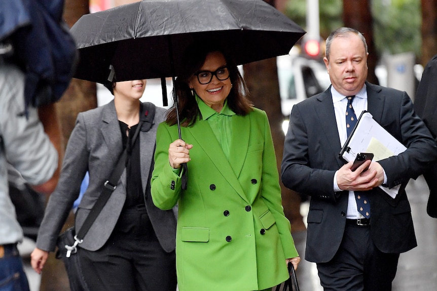 Lisa Wilkinson, dressed in a bright green suit, holds an umbrella above her head.