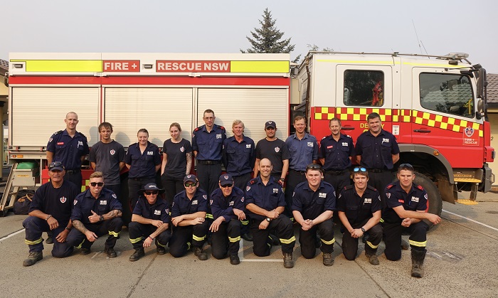 a fire truck behind a group of firefighters in blue uniforms