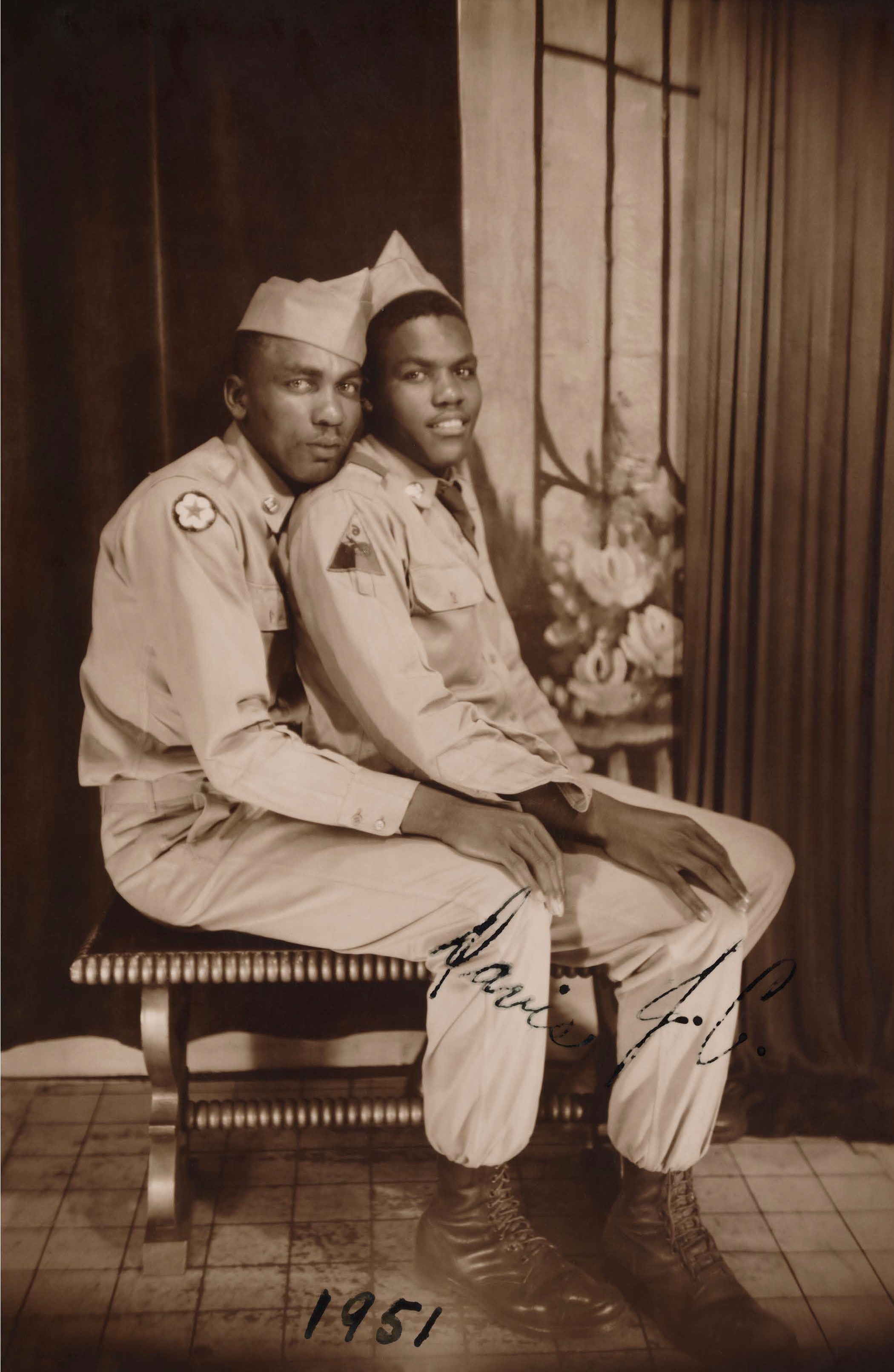 Dos hombres uniformados están sentados abrazados en un banco. La foto está fechada en 1951.