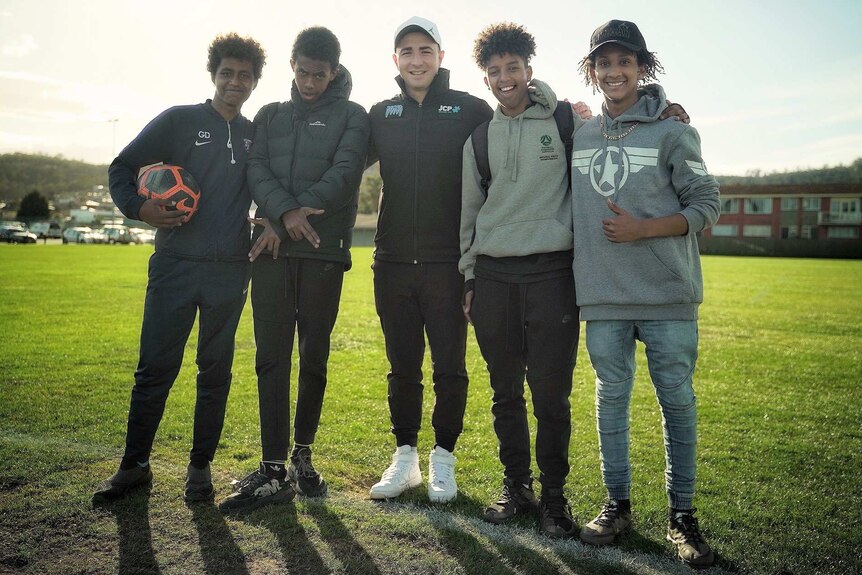 Will Smith stands with two teenage boys either side of him at a soccer field in Hobart.