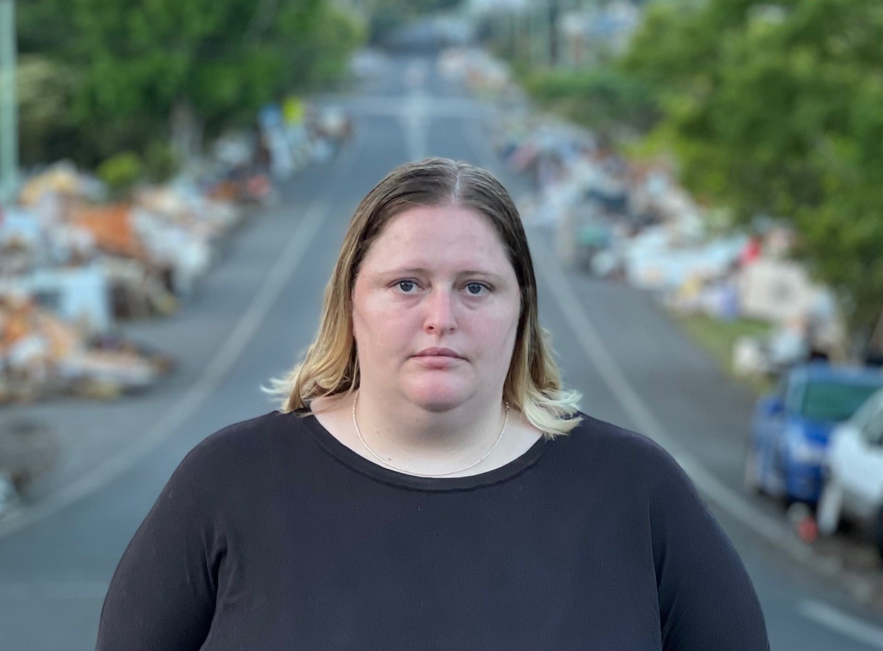 A woman stands on a street with rubbish on either side.