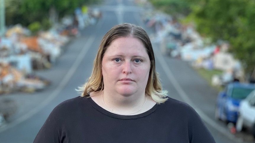 A woman stands on a street with rubbish on either side.