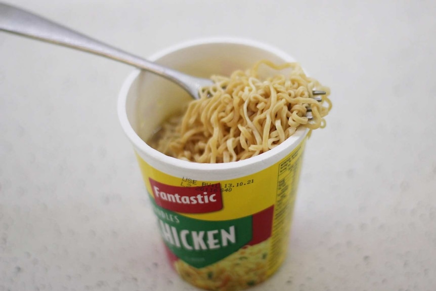 A plastic cup of two-minute noodles with a fork in the cup.