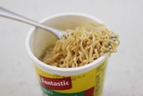 A plastic cup of two-minute noodles with a fork in the cup.
