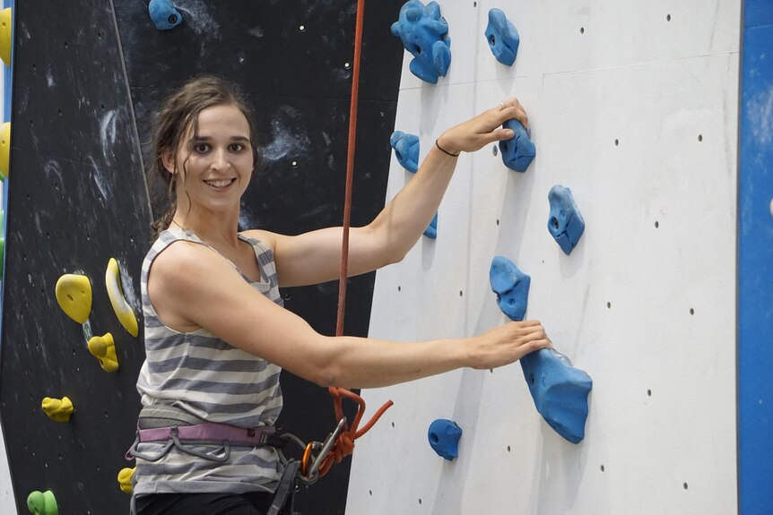 Araminta McLennan sourit en escaladant un mur aux pieds bleus.