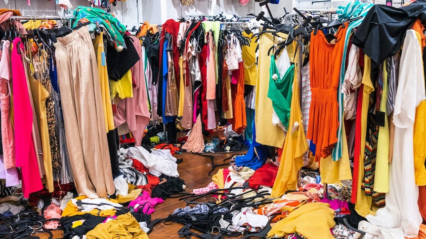 Mountains of colourful clothes strewn over racks in a room
