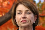 Anna Bligh in one of the Parliament House courtyards, with a tree in the background which has red leaves.