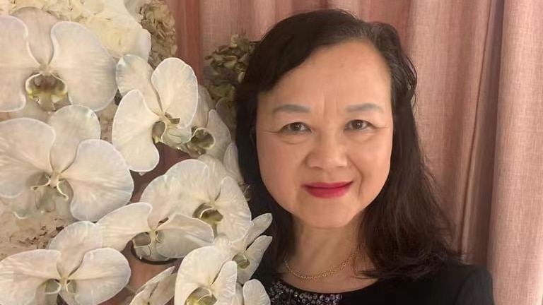 A smiling woman with red lipstick and black hair in front of white flowers. 