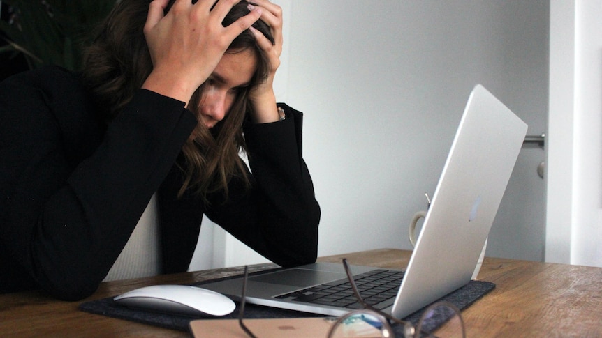 A woman with an open laptop puts her head in her hands