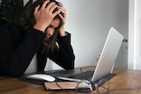 A woman with an open laptop puts her head in her hands