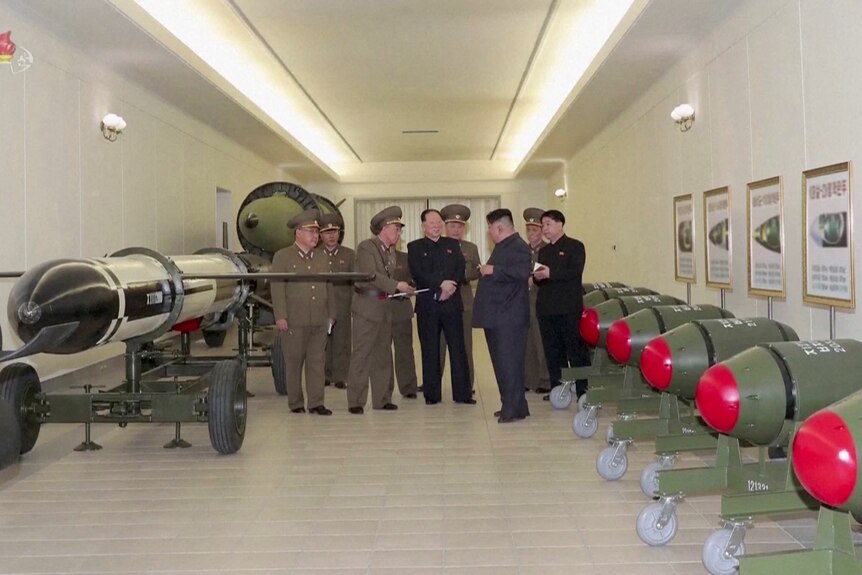 A group of men standing at the far end of a room with big green and red round missiles lined up against the wall