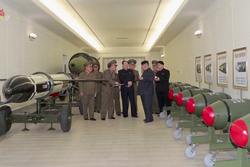 Группа мужчин, стоящих в дальнем конце комнаты с большими зелеными и красными круглыми ракетами, выстроенными в ряд у стены.