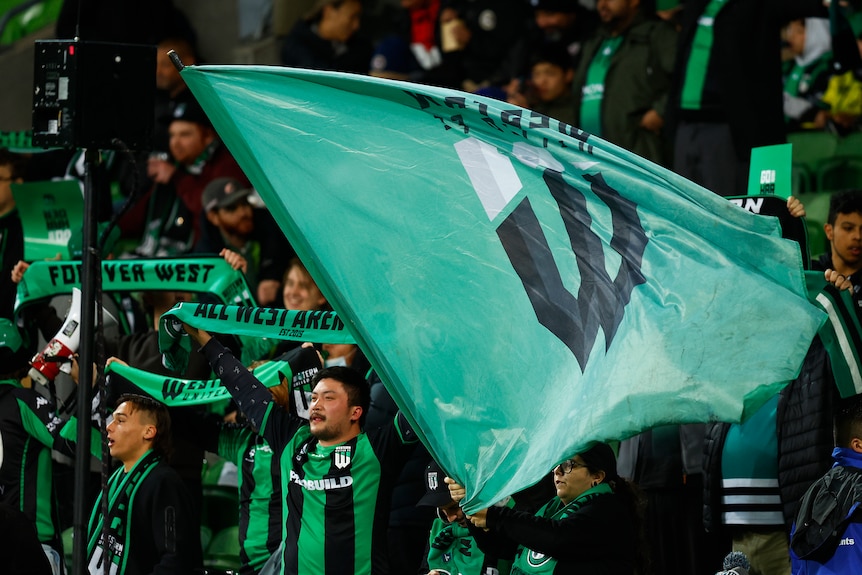 A green Western United flay is waved in front of supporters holding up green scarves