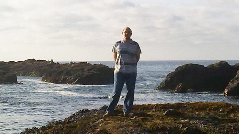 A man stands on a rocky shore.
