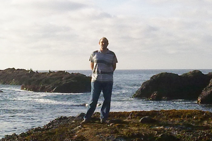 A man stands on a rocky shore.