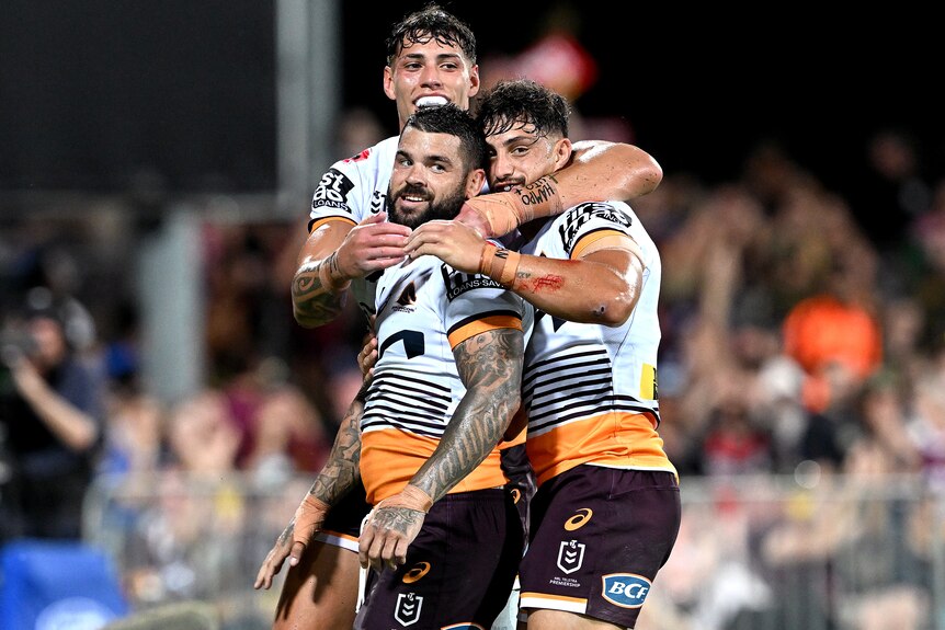 Three Brisbane Broncos NRL players embrace as they celebrate a try.