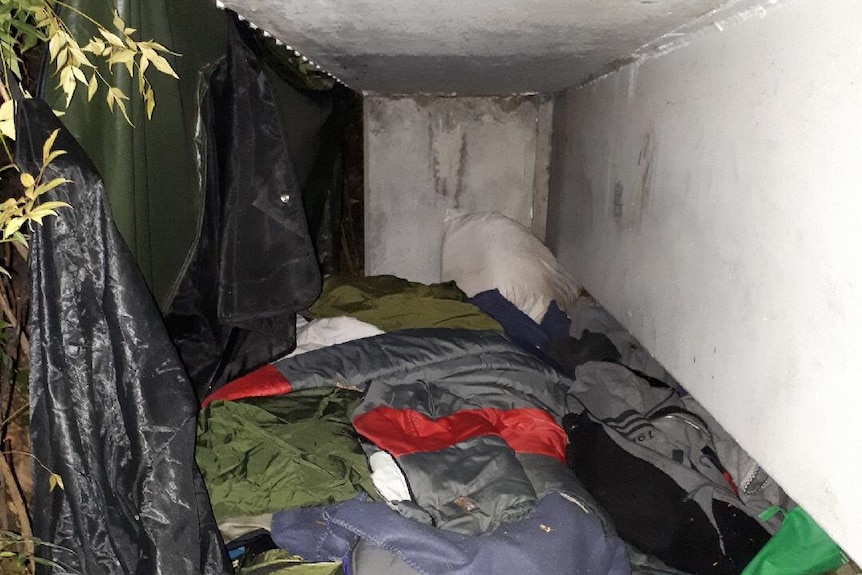 A nook underneath a building with a sleeping bag and plastic tarp to keep dry.