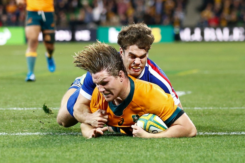 Michael Hooper dives over the line with a French player on his back