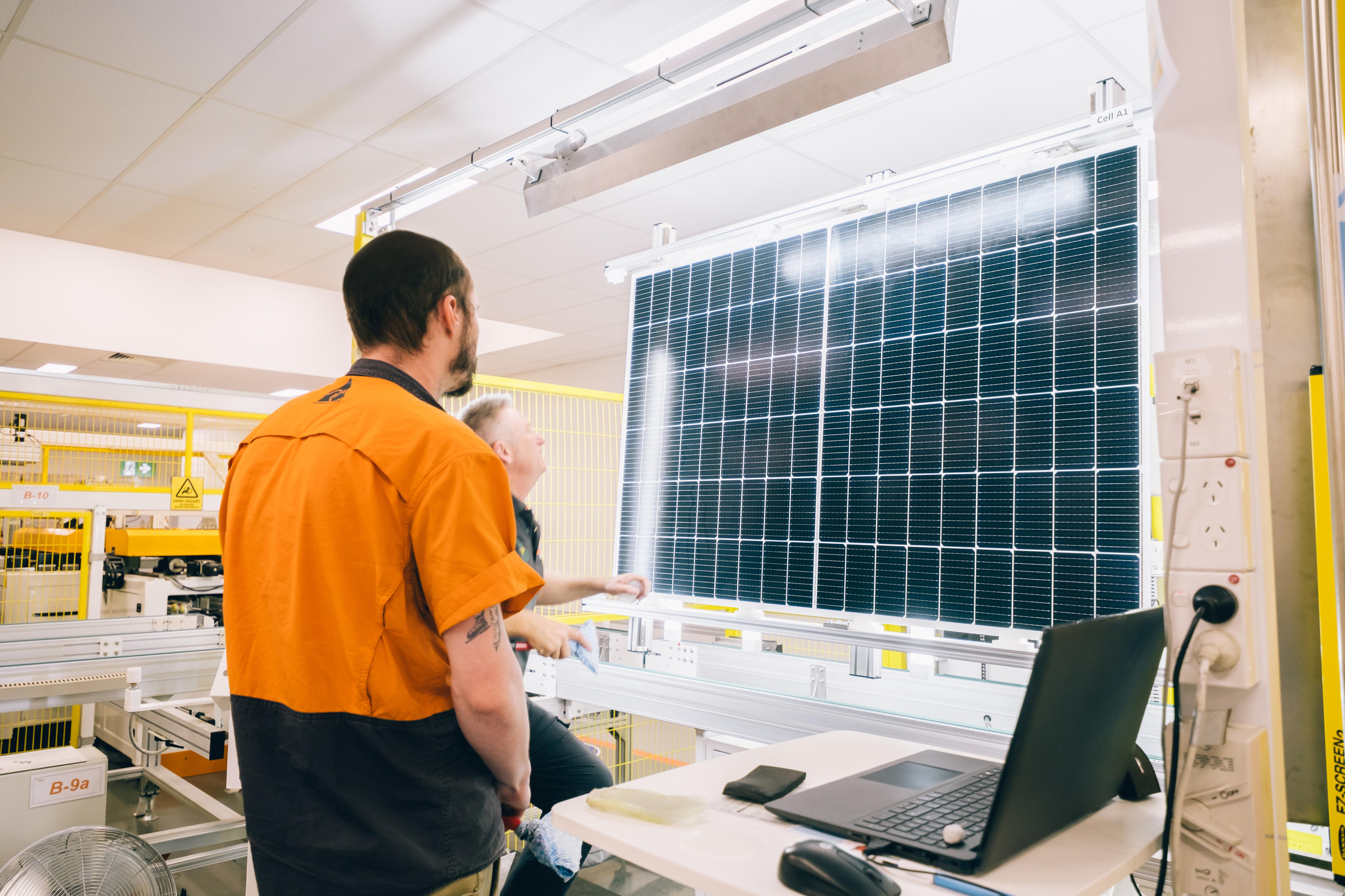 Two men look at a photovoltaic cell that's suspended under lights for inspection