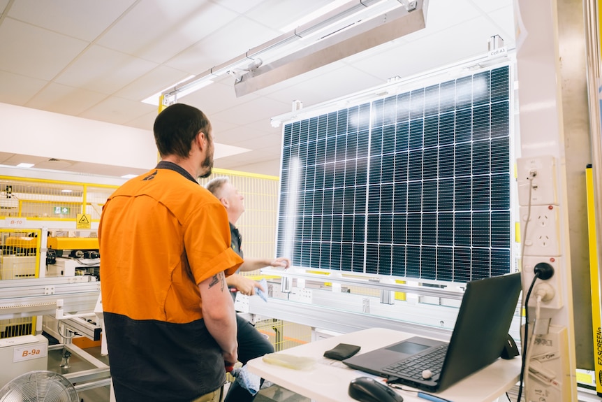 Two men look at a photovoltaic cell that's suspended under lights for inspection