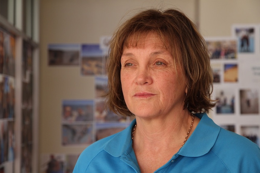 A woman with chin length auburn hair, wearing a blue shirt, looks past the camera.