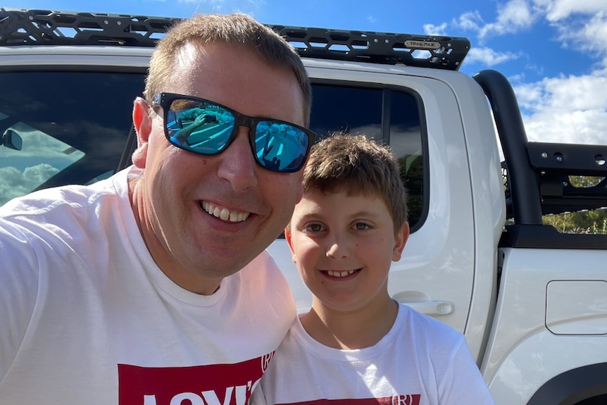 James Mancey and his son Angus standing in front of a car wearing matching T-shirts. 