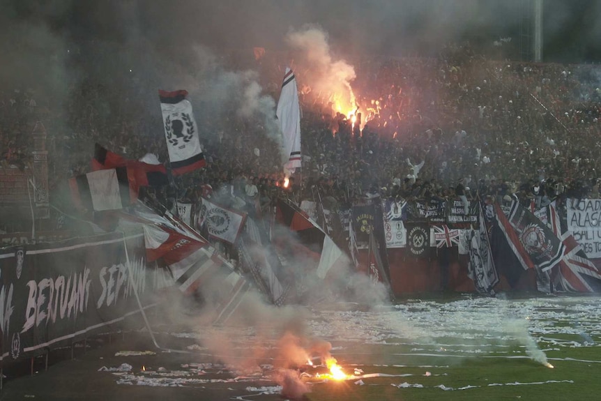 Football fans throw streamers and light flares in the stands.