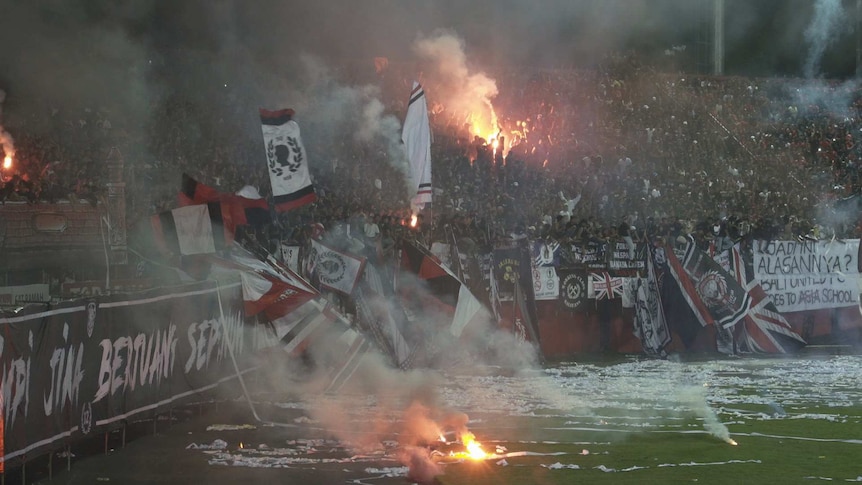 Football fans throw streamers and light flares in the stands.