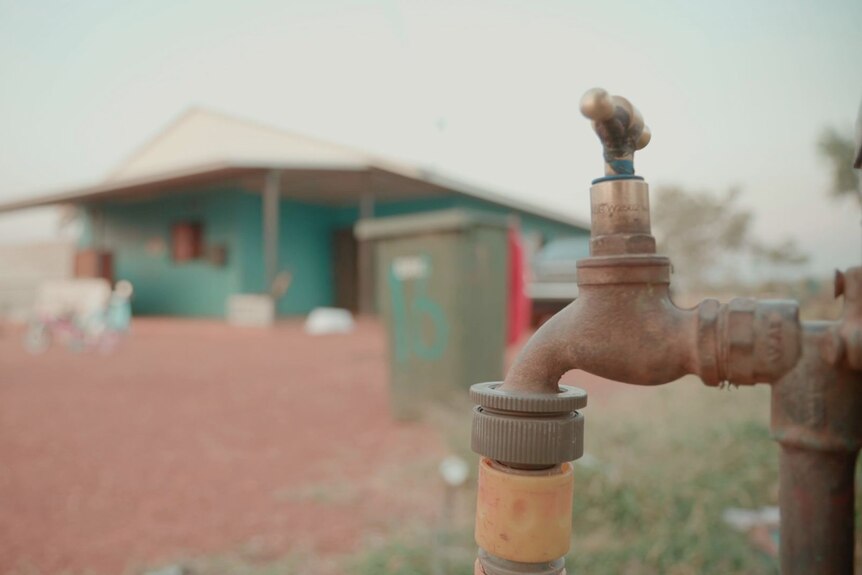 A tap with a home in the background. 