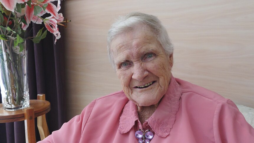 An elderly lady seated inside smiles to camera
