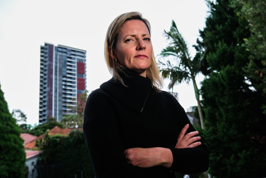 A woman with her arms crossed and a tall building in background