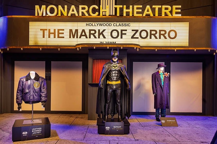 A display of Batman costumes in front of a set designed to look like a theatre