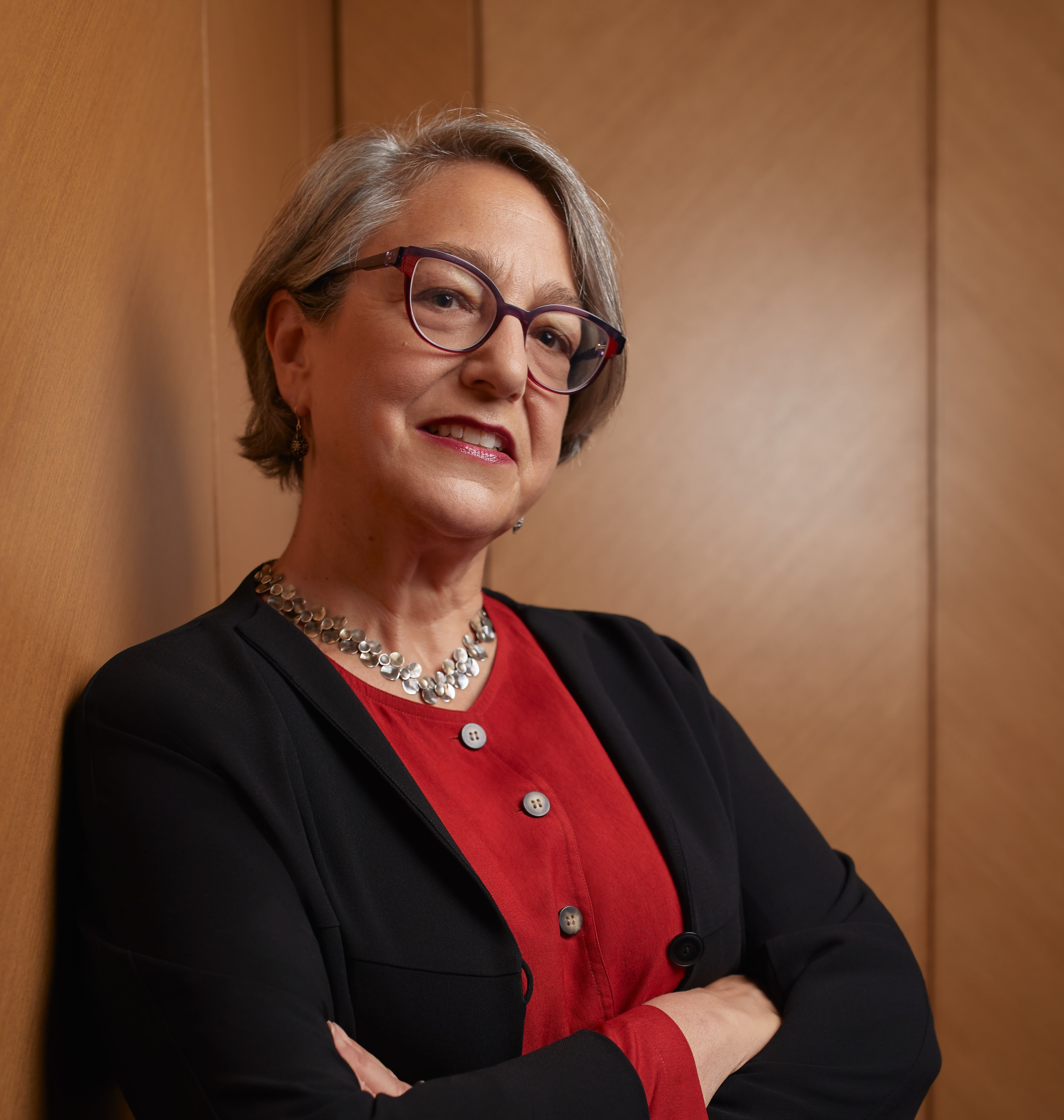 Portrait of an older woman with short grey hair. She's got a red top on and a black jacket.