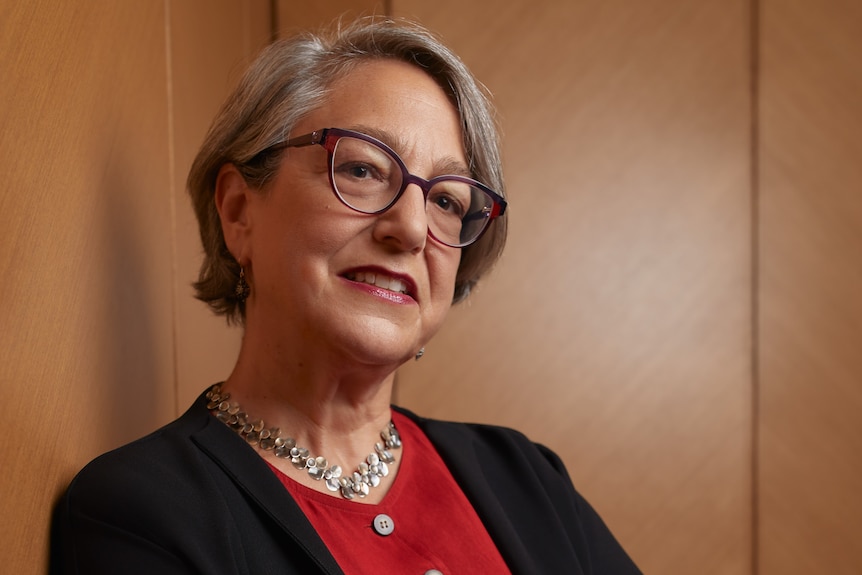 Portrait of an older woman with short grey hair. She's got a red top on and a black jacket.