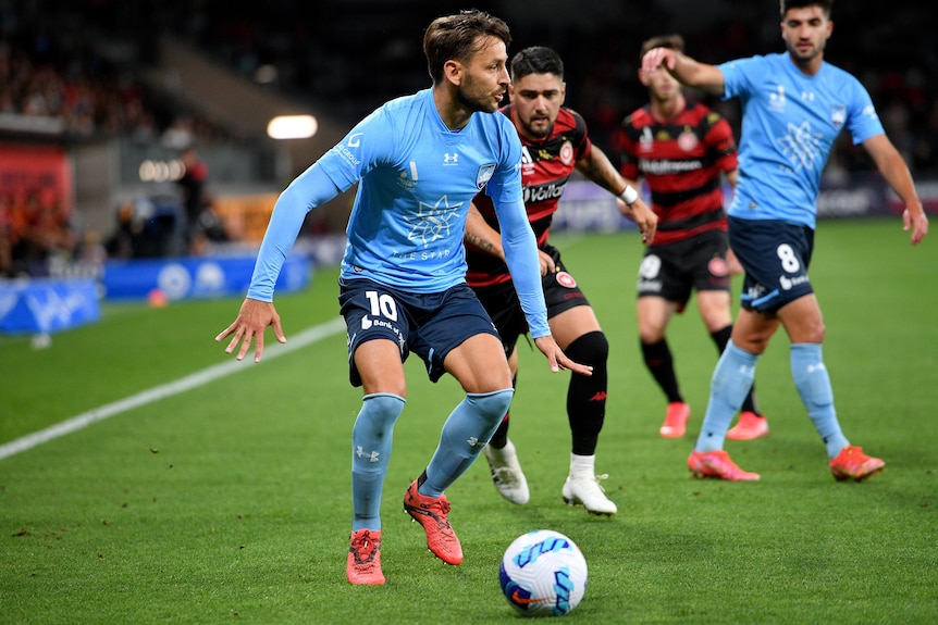 Football player controls the ball at his feet near defenders.